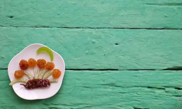 Vietnamese food for Vietnam Tet holiday, also lunar new year of Asia, colorful preserved fruit as kiwi, damson jam, or coconut jam set up on white plate with green wood background make art