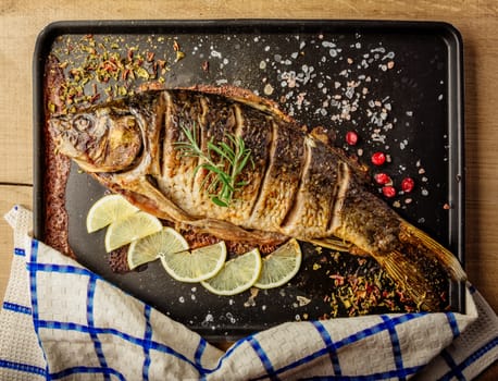baked carp with spices and lemon on black pan