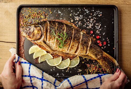 chef holds baked carp with spices and lemon on black pan