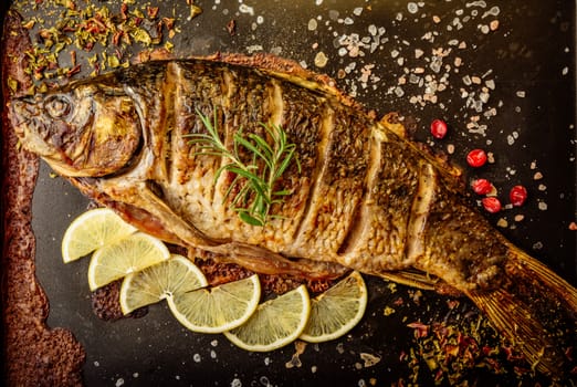 baked carp with spices and lemon on black pan