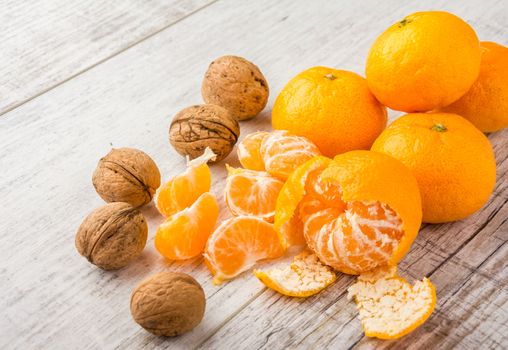 tangerines, peeled tangerine, tangerine slices and walnuts on a white wooden table