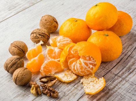 tangerines, peeled tangerine, tangerine slices and walnuts on a white wooden table