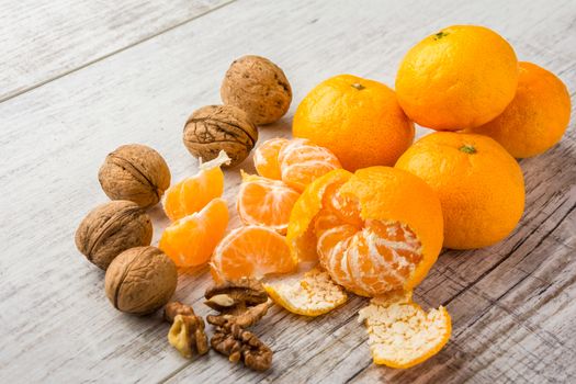 tangerines, peeled tangerine, tangerine slices and walnuts on a white wooden table