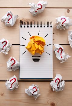 Bright paper light bulb on a notepad between crumpled pieces of paper with question marks