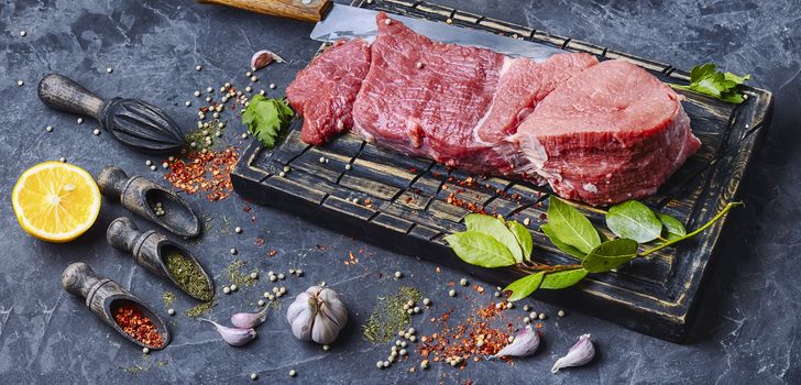 Raw beef steak and laurel branch on cutting board