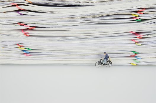 Stack of documents with colorful clips and miniature people is bicycling on white background.