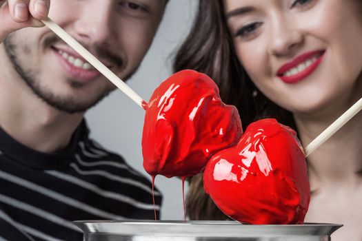 Fondue of love, loving couple dips chocolate hearts in red glaze