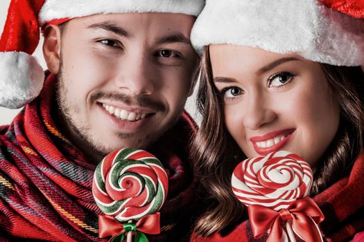 Young happy funny couple in christmas santa hats with lollipops