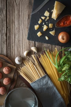 Ingredients for cooking spaghetti, meatballs with cheese and fresh herbs on the old table vertical