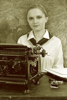 Nice girl for a vintage typewriter in retro style on background of old wall