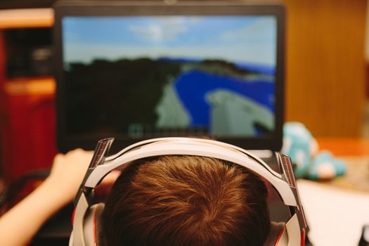 Boy wearing headphones playing online games on a laptop.