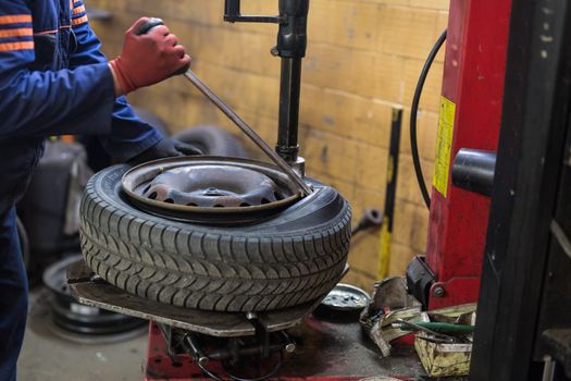 Professional auto mechanic replacing tire on wheel in car repair workshop.
