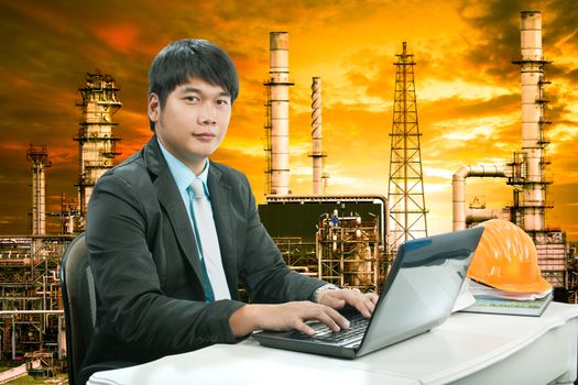 portrait young engineering  man sittin and working on laptop computer against oil refinery industry estate