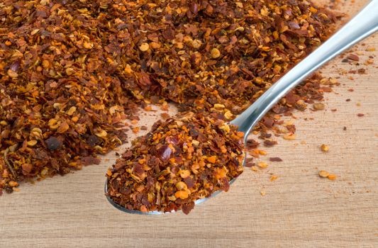 Organic hot red chili flakes made from organically grown whole red chillies on wooden cutting board background