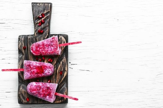 three pomegranate ice creams on sticks on the kitchen board