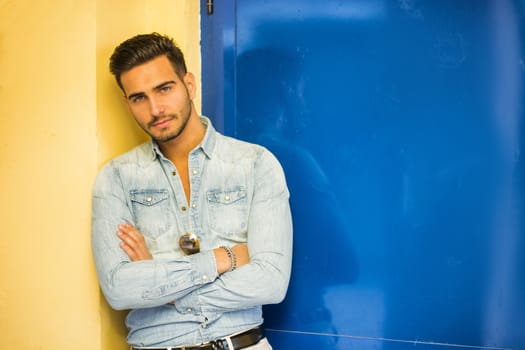 Attractive young man sitting against colorful wall, looking at camera