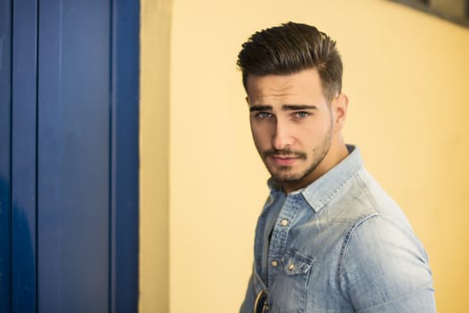 Attractive young man sitting against colorful wall, looking at camera