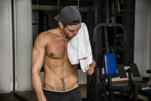 Muscular young man drying sweat from his face with a towel after workout in a gym