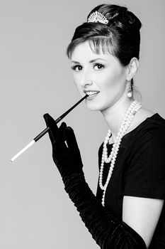 Portrait of a beautiful young woman in retro style with cigarette in mouthpiece in the image of the famous actress Audrey Hepburn. Black and white photography