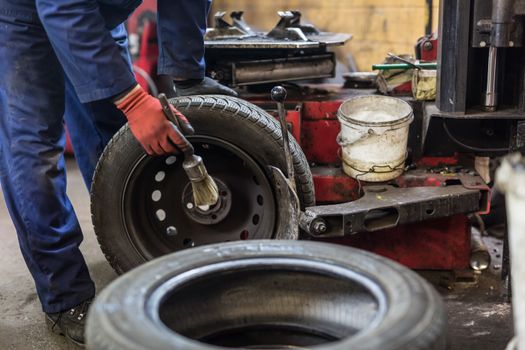 Professional auto mechanic replacing tire on wheel in car repair workshop.