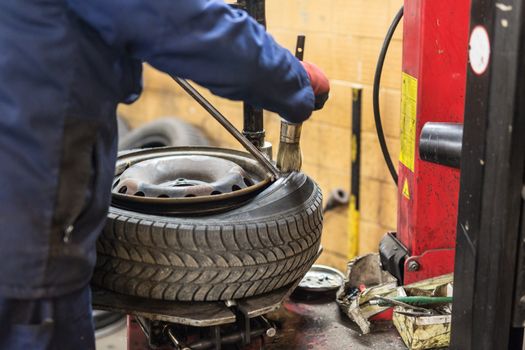 Professional auto mechanic replacing tire on wheel in car repair workshop.