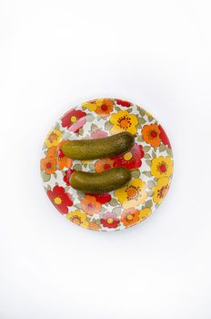 Overhead shot of on tow cucumbers on a flowery orange and red  dish, on white.