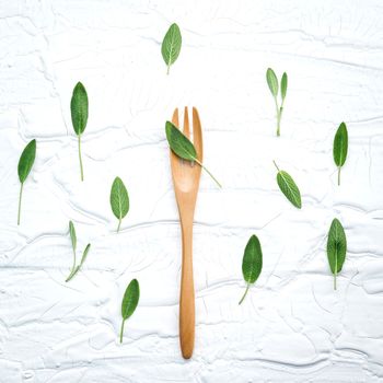Closeup  fresh sage leaves  with fork on white wooden background . Alternative medicine fresh salvia officinalis with flat lay.