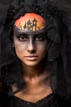 Halloween devil's bride. Portrait of young woman in dark artistic image with scary makeup, veil and terrible picture on her forehead.