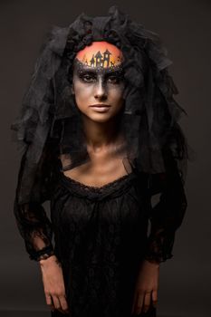 Halloween devil's bride. Portrait of young woman in dark artistic image with scary makeup, veil and terrible picture on her forehead.