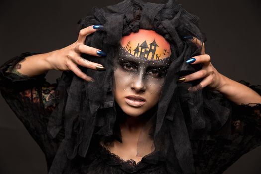 Halloween devil's bride. Portrait of young woman in dark artistic image with scary makeup, veil and terrible picture on her forehead.