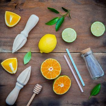 Mixed fresh citrus fruits and orange leaves background. Ingredients for summer citrus juice with juicer and glass bottle .Fresh lemons, lime and oranges set up on shabby wooden table with flat lay.