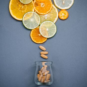 Healthy foods and medicine concept. Bottle of vitamin C and various citrus fruits. Mixed citrus fruits sliced lime,orange and lemon on gray background flat lay.