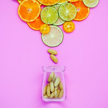 Healthy foods and medicine concept. Bottle of vitamin C and various citrus fruits. Citrus fruits sliced lime,orange and lemon on light pink background flat lay.