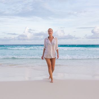 Woman wearing white loose tunic over bikini on Mahe Island, Seychelles. Summer vacations on picture perfect tropical beach concept.