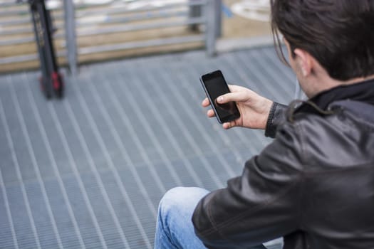 Handsome young man standing outdoors in urban environment on metal stairs, using cell phone