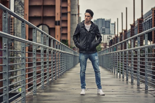 Handsome young man standing outdoors in urban environment on metal stairs, looking at camera