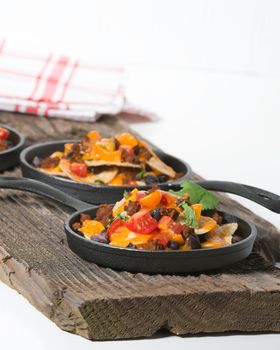 Colorful nachos served in individual cast iron fry pans.