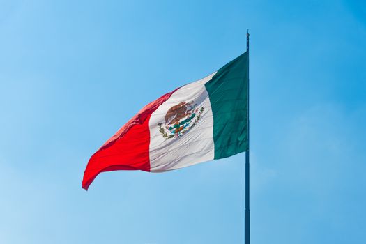 Flag of Mexico in the wind on a sunny day against the blue sky.