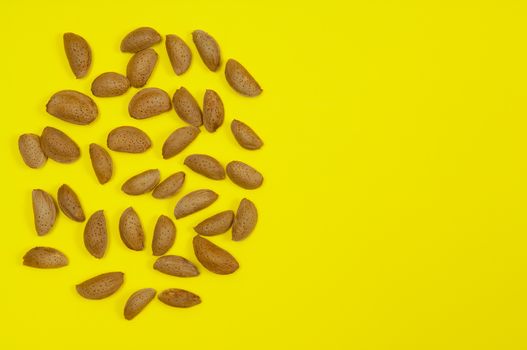 A pile of in shell raw almond on yellow background with copy space