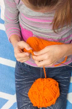 Top view of the child who knits with needles scarf orange thread