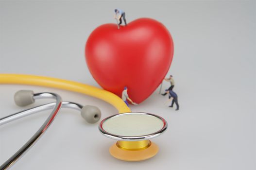 Miniature people are caring the heart and stethoscope put on table.