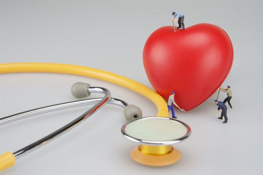 Miniature people are caring the heart and stethoscope put on table.