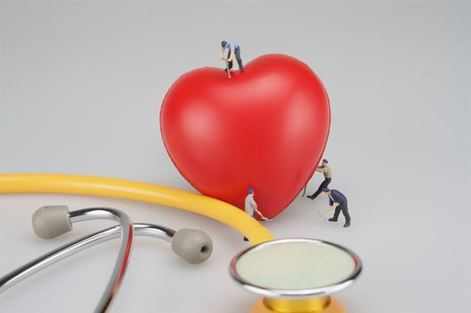 Miniature people are caring the heart and stethoscope put on table.