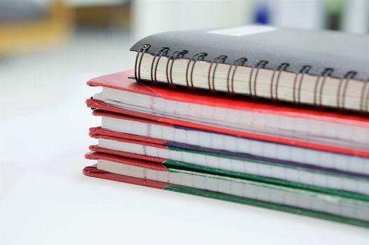 Notebook and stack of report book on desk with office background.