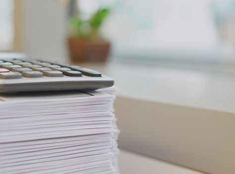 Pile of printout and calculator organised on desk at office                             