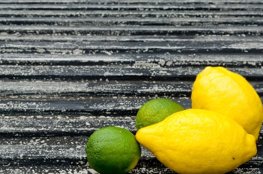 Lemon and lime arrangement on old black textured metal surface