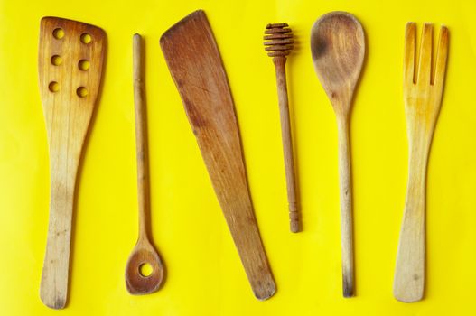 Old wooden spoons and stirrers on yellow background, kitchen utensils