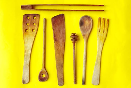 Old wooden spoons and stirrers on yellow background, kitchen utensils