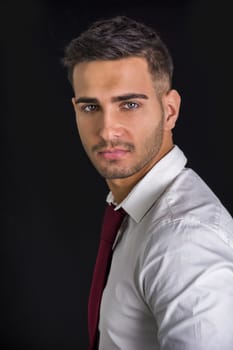 Handsome young man in in white shirt and red neck tie posing on dark background in studio