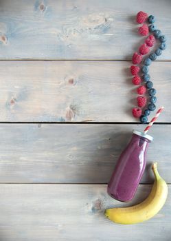 Berry flavoured smoothie in a bottle over a wooden background with copyspace